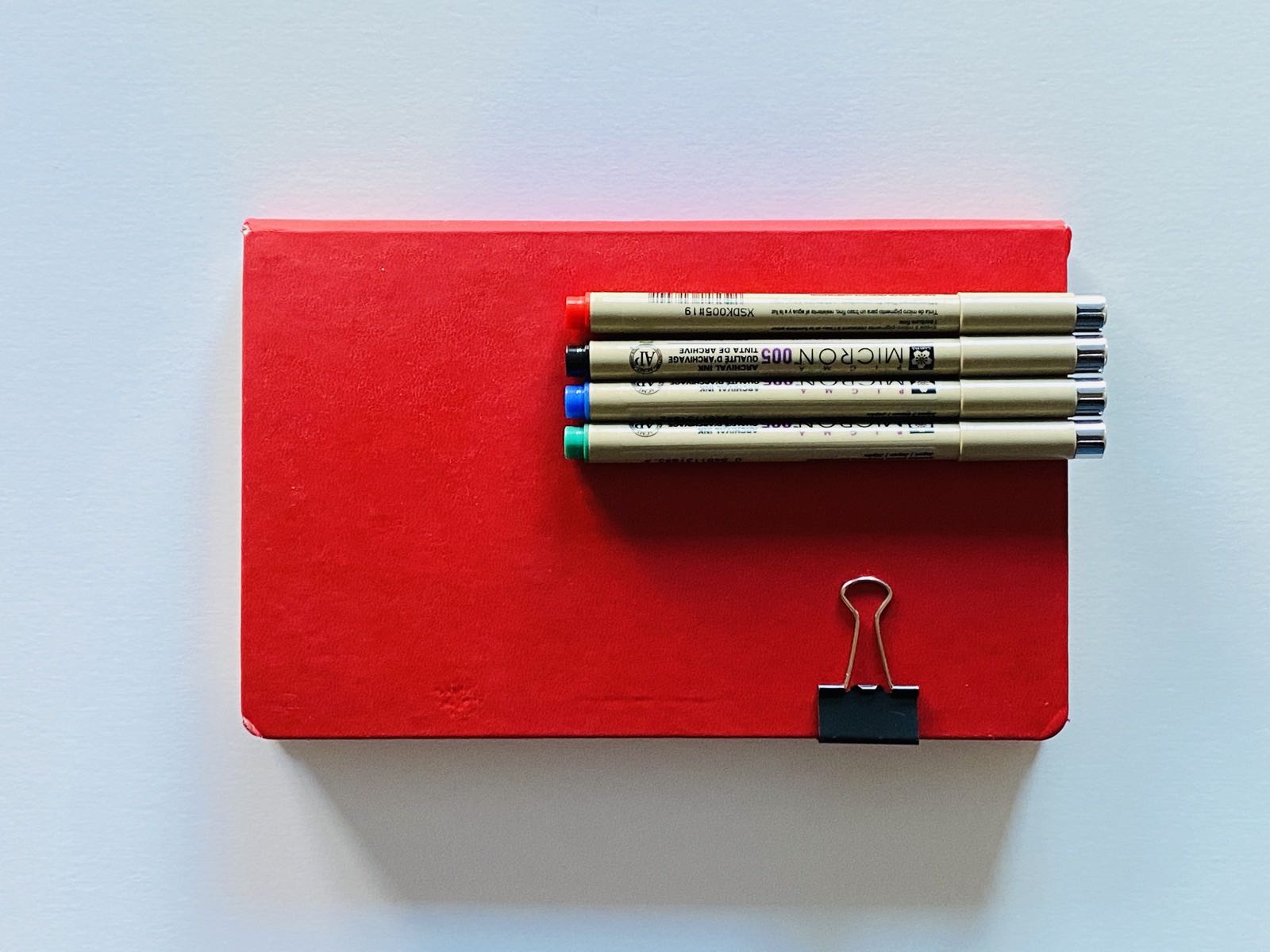 Red Moleskine notebook with four Micron pens attached.